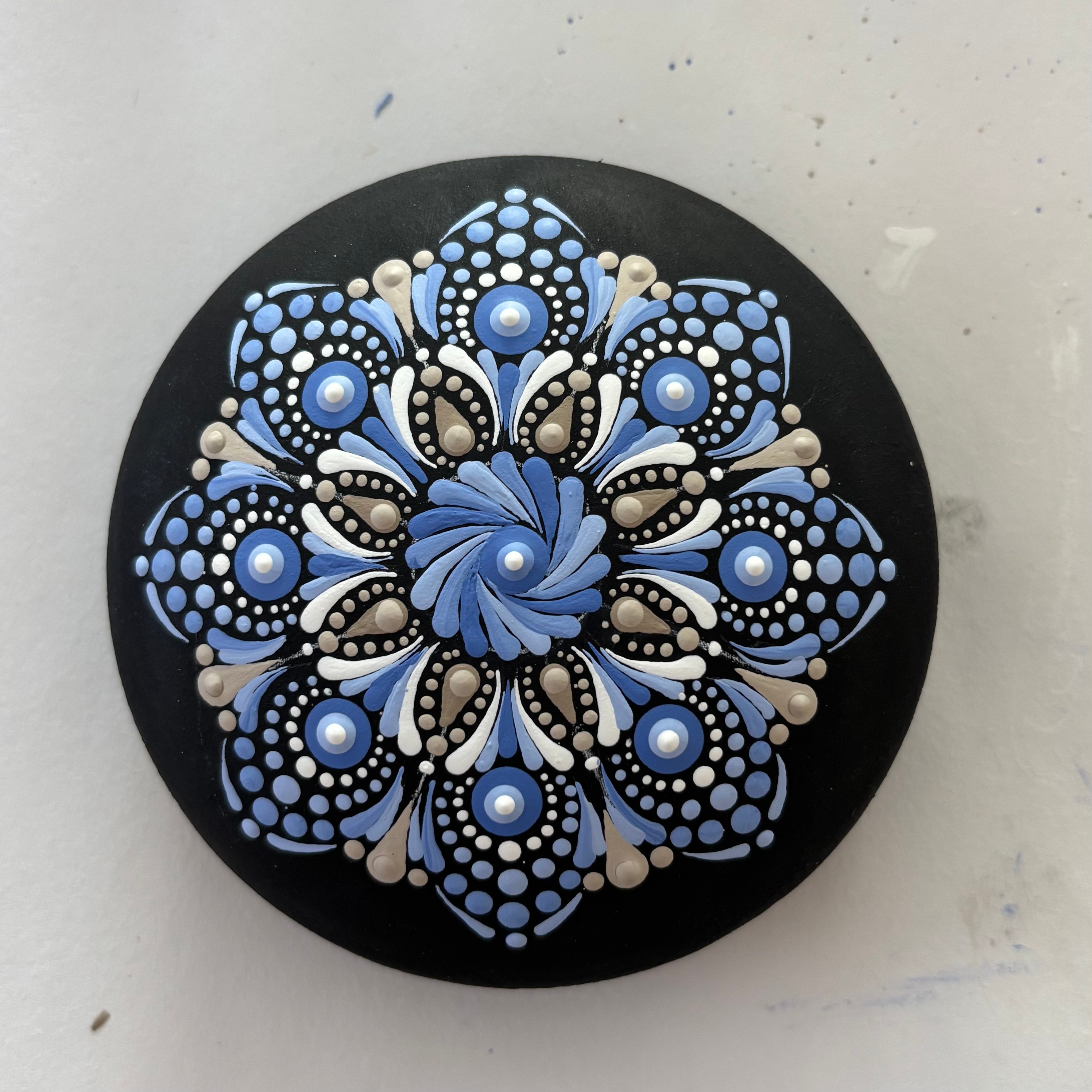 Blue and white mandala dot painting on black circular surface